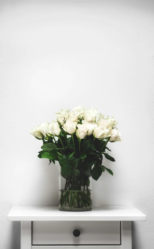 white roses in a vase on a small white shelf