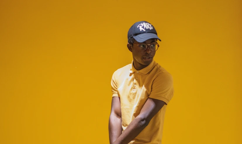 man wearing a yellow t - shirt and hat leaning against a wall