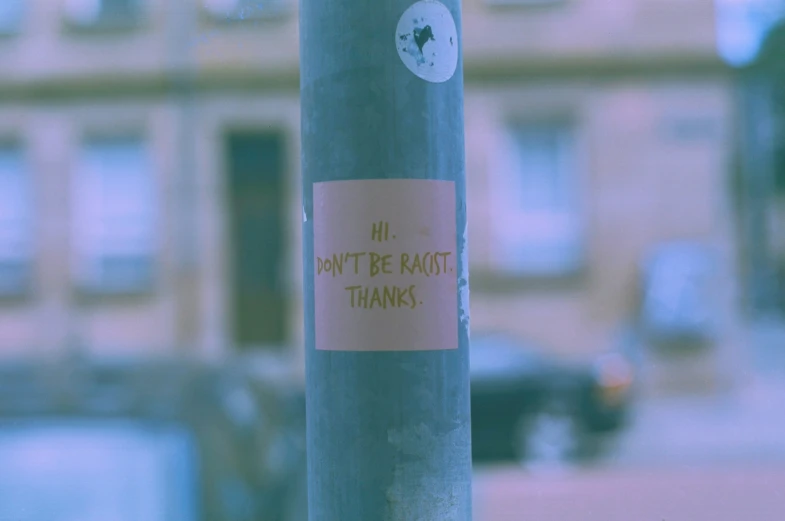 the sticker says don't be racist thanks on a pole