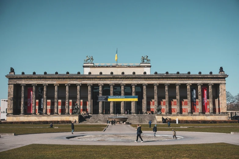 people walking in front of a building with large pillars and flags