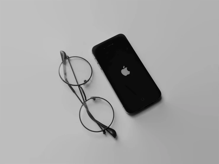 an iphone, reading glasses and pen are sitting on a gray background