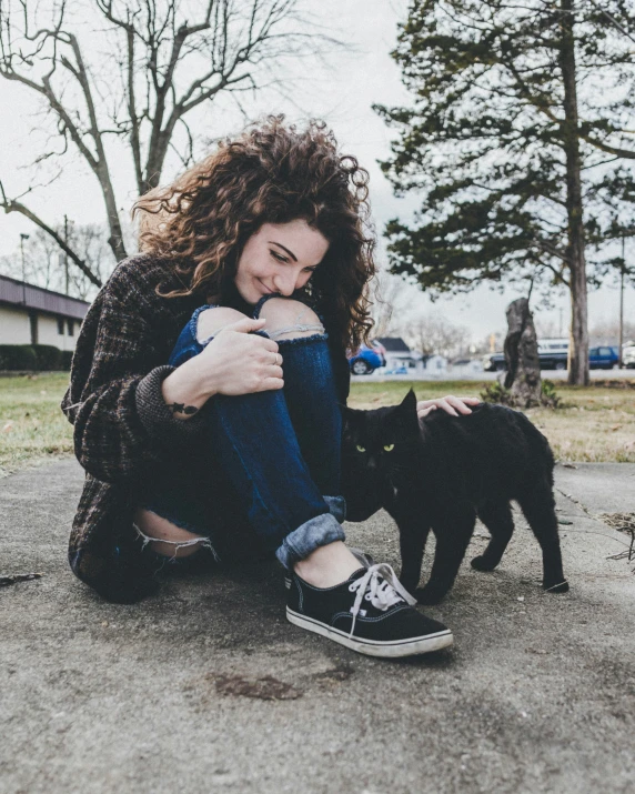 woman is crouched down with a black cat