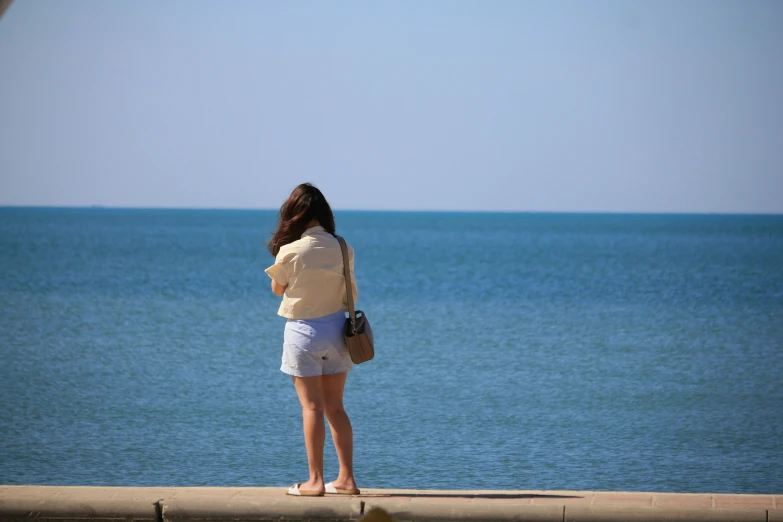 a woman wearing shorts is looking at the ocean
