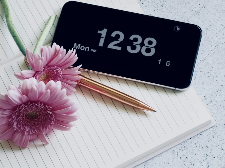 a black clock and two pink flowers are on a note pad