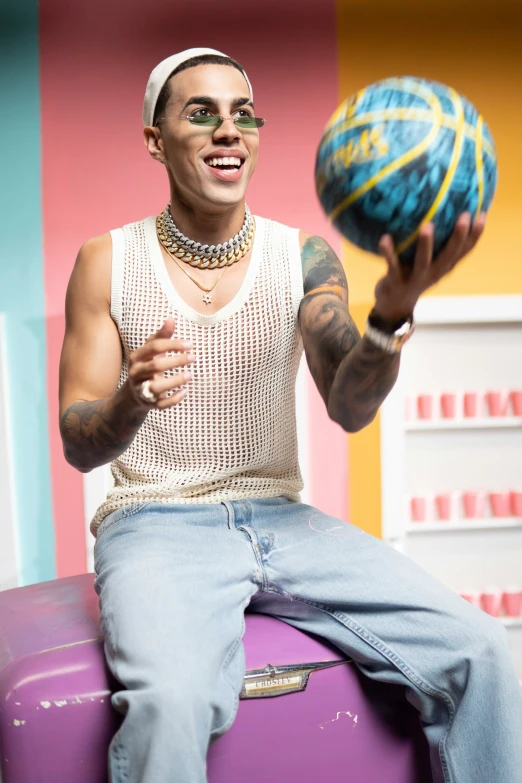 a man with a mohawk is spinning a ball on top of purple luggage