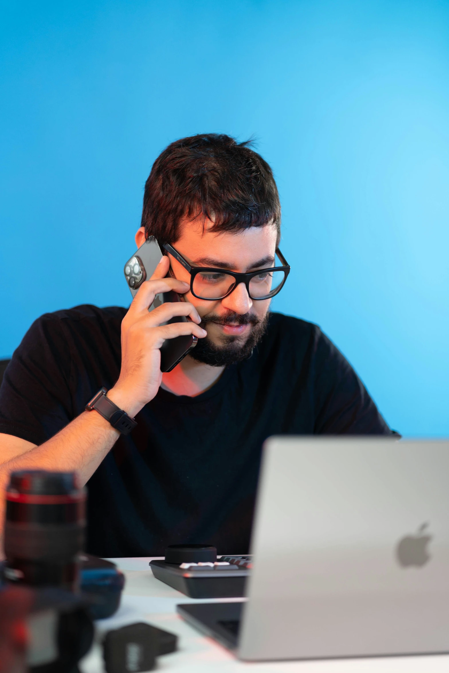 a man in glasses talking on a cell phone near his laptop