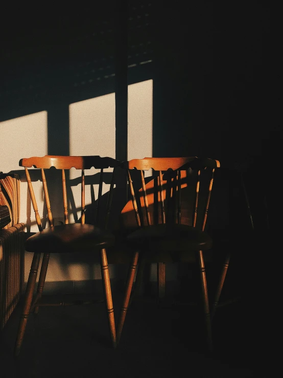 two wooden chairs sitting in front of a window with the blinds drawn down