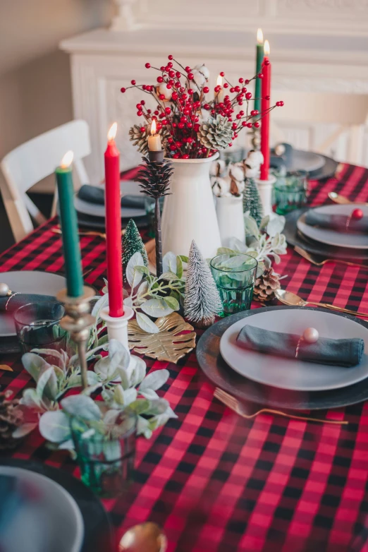 a holiday dining room decorated with red and green placemats, evergreens, red candles, and dishes