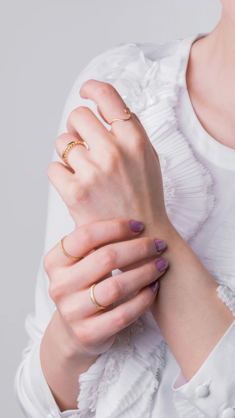 a woman in white shirt and gold celet holding onto her hands