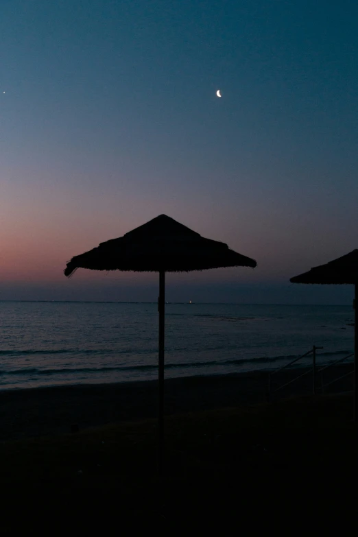 a couple of umbrellas on a beach at dusk