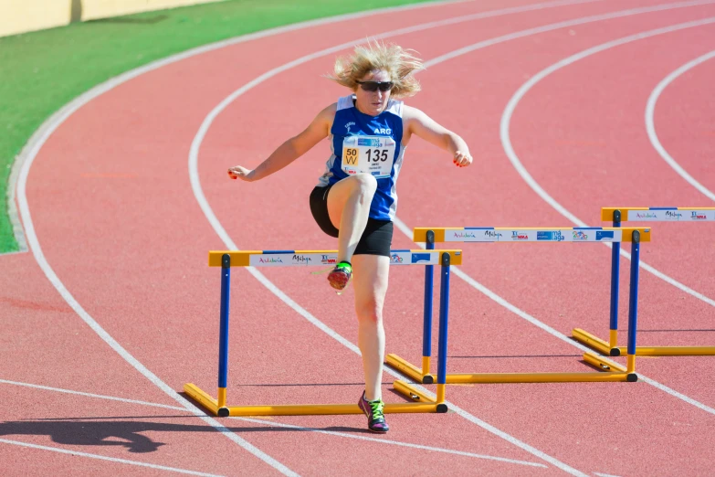 an athlete leaps over a hurdle on the track