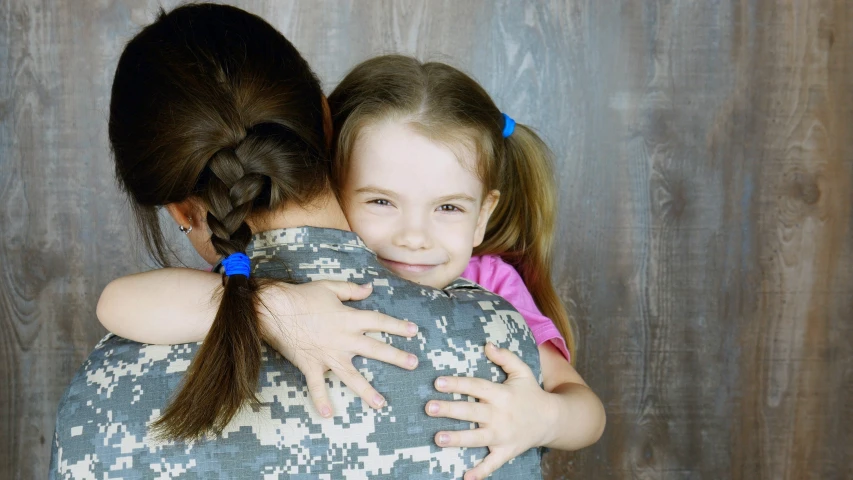 the little girl hugs the military woman from behind