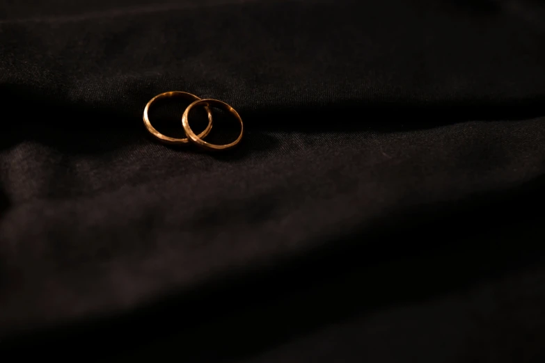 two golden rings laying on a black cloth