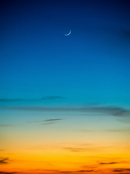 a very distant moon, almost obscured by the moon on a very blue sky