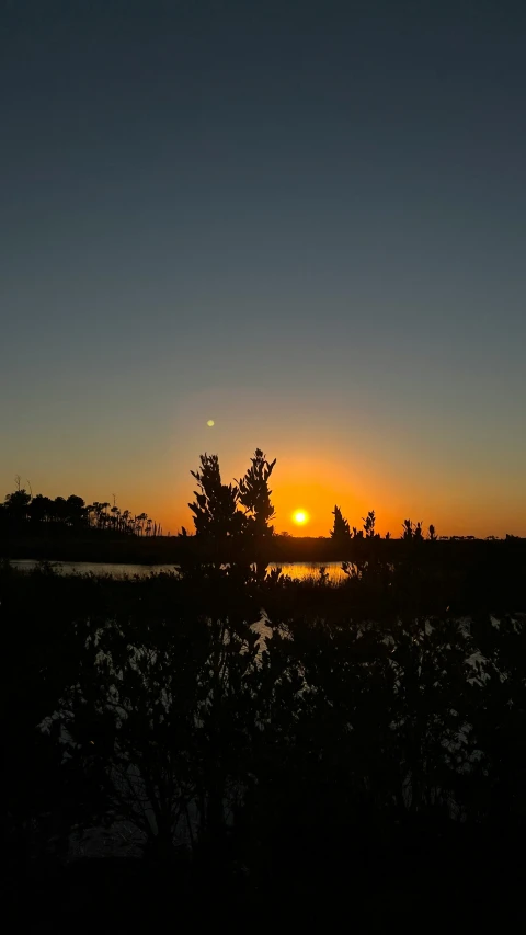 the sun set over a body of water with trees