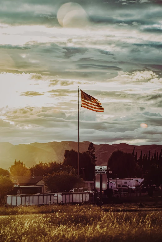 an american flag flies in the foreground, in front of a rural setting