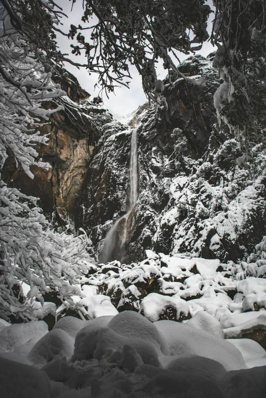 a waterfall with snow covered rocks and snow on the ground