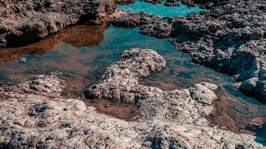 a sandy shore filled with water surrounded by lots of large rocks