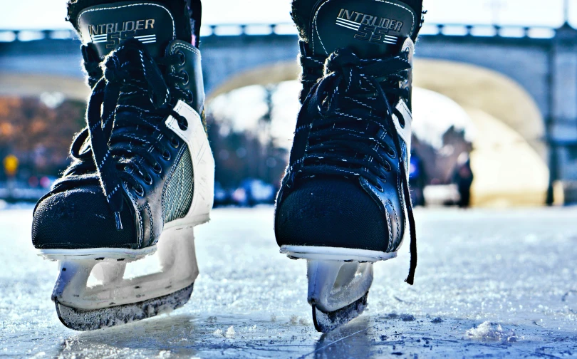 a person wearing black shoes standing on some ice skates