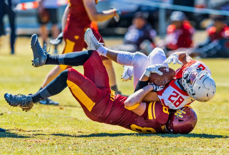 two football players collide on each other while holding a football