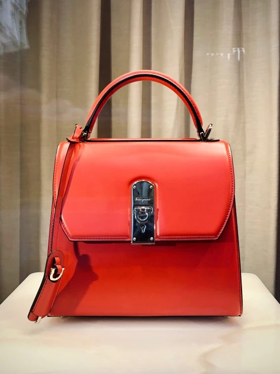 red purse sitting on a table top with curtain in the background