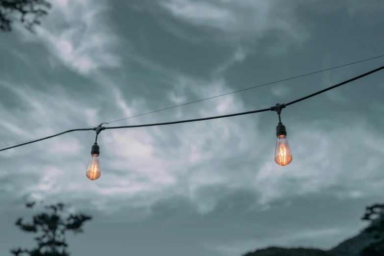 light bulbs on an electrical wire in front of clouds