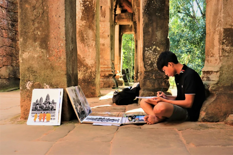 a little boy sitting down in front of some old pillars