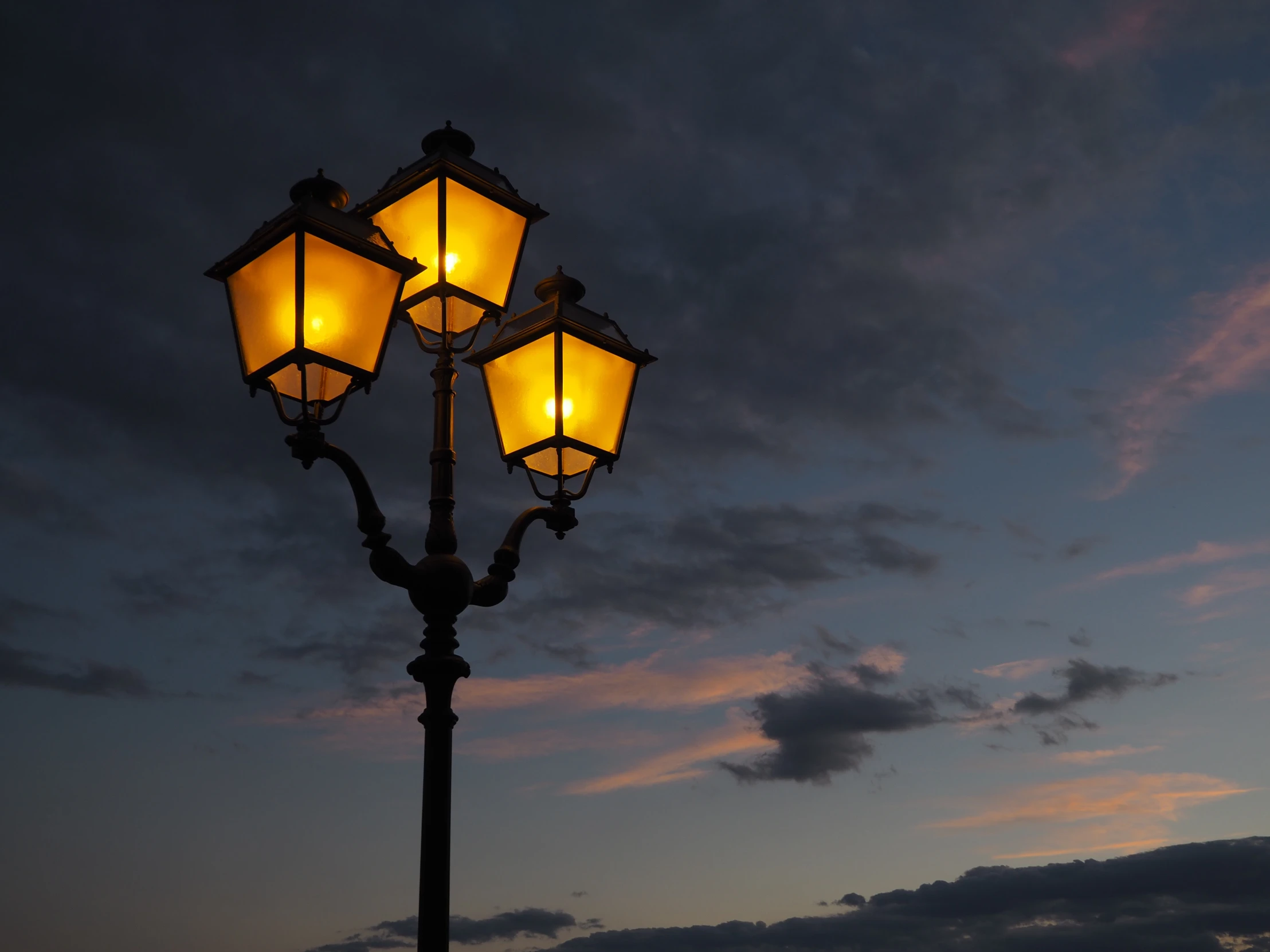 three street lights sitting next to each other against a cloudy sky