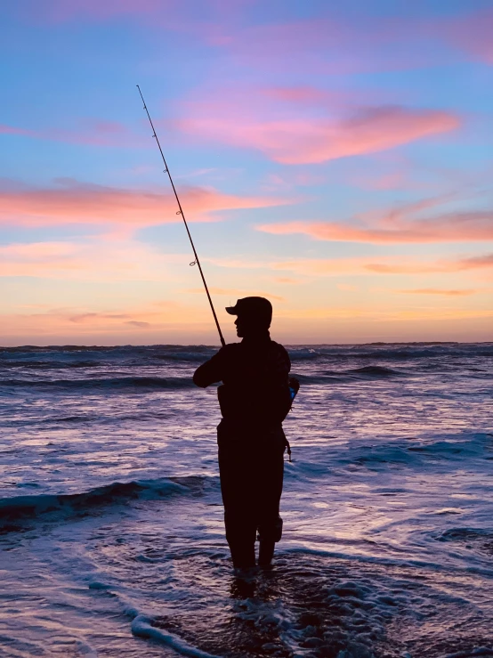 a man holding a fishing pole while standing in the ocean