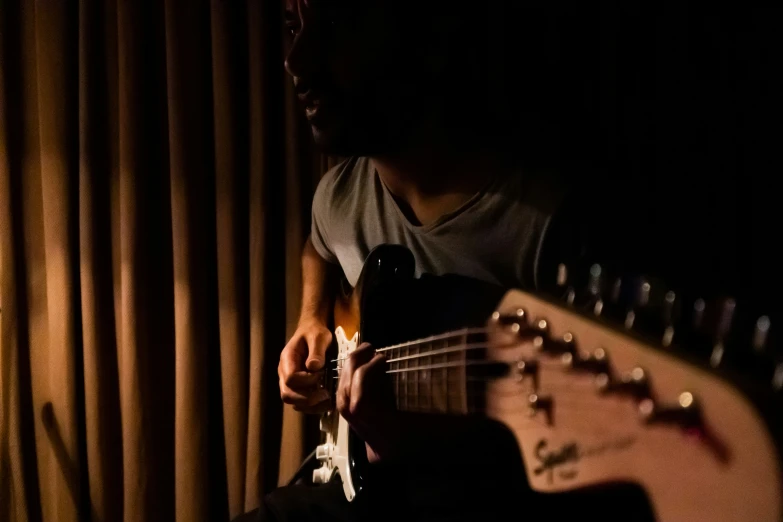 a close up of a person playing a guitar with dark curtains