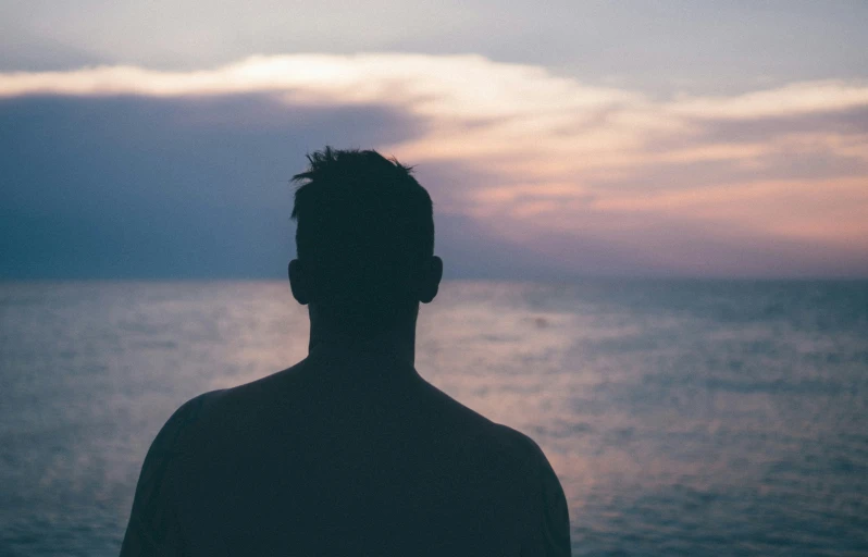 a person looking at the water with a sky and clouds in the background