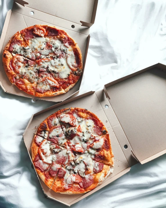 two pizzas in separate boxes sitting on a bed