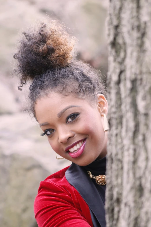 a woman with an afro up in a mohawk standing next to a tree