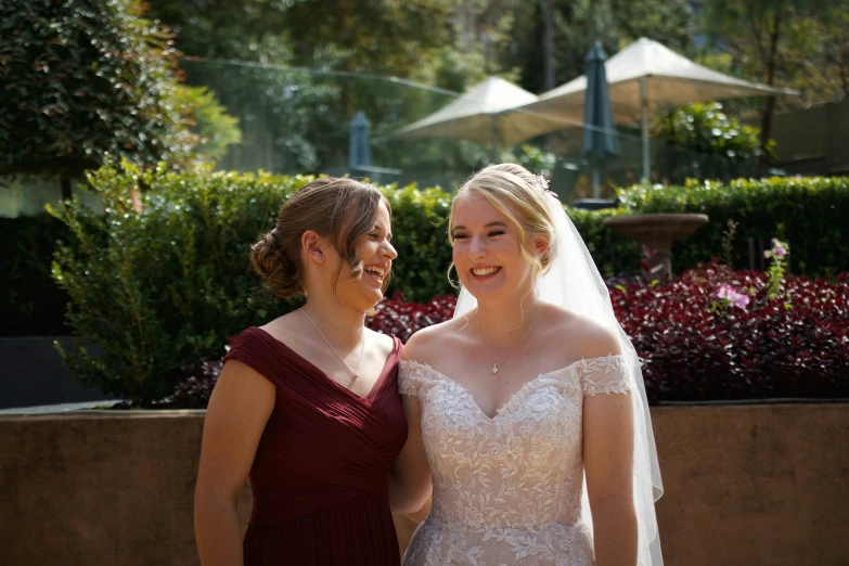 two women in wedding dresses stand together while talking