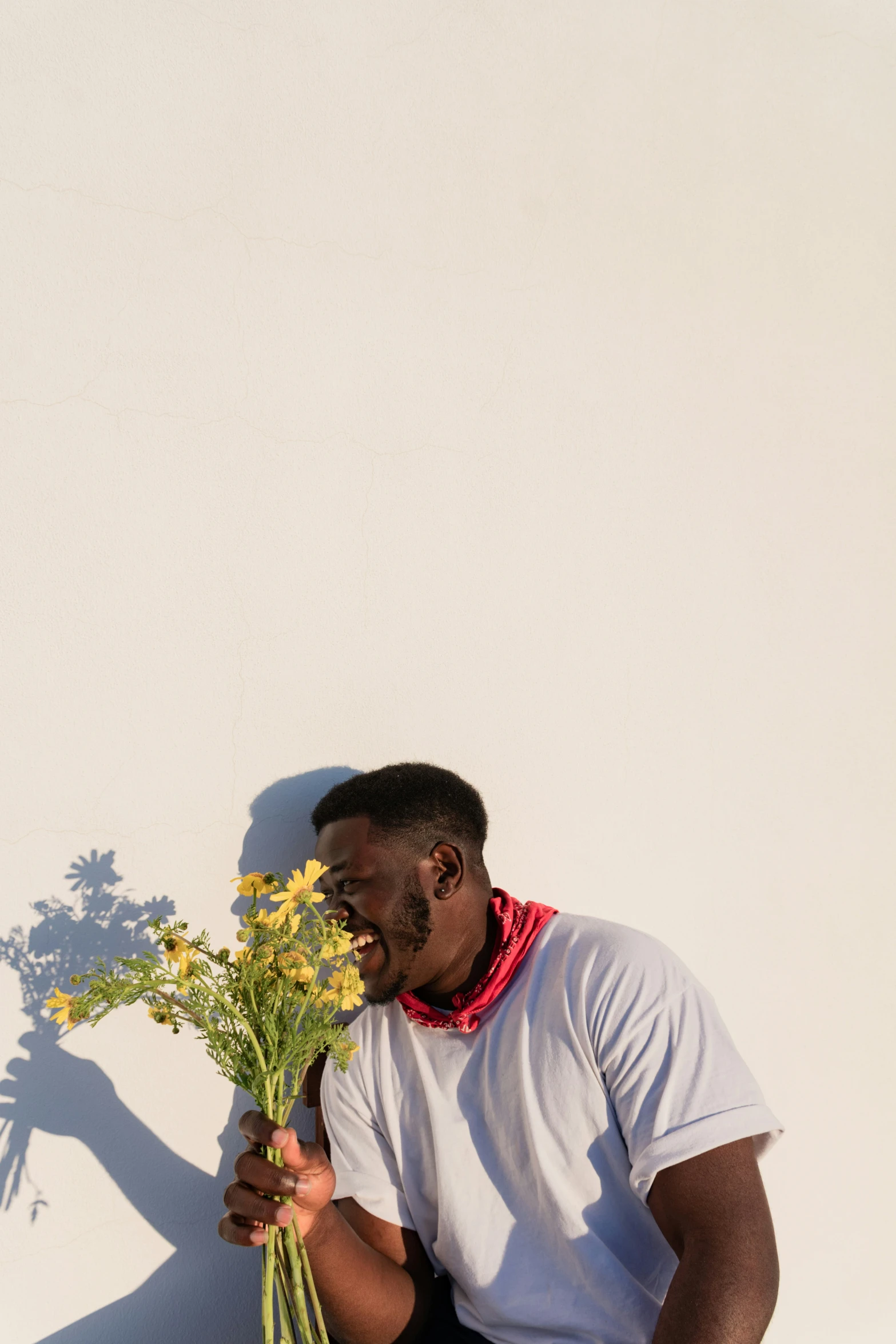 man holding yellow flowers against white wall in the sun