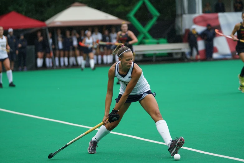 women's field hockey player in blue and white uniform and ball on field