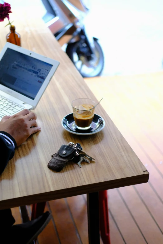 someone is sitting at a wooden table using a laptop and cell phone