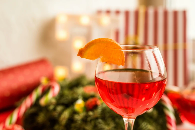 a glass with liquid, orange slice and candy canes