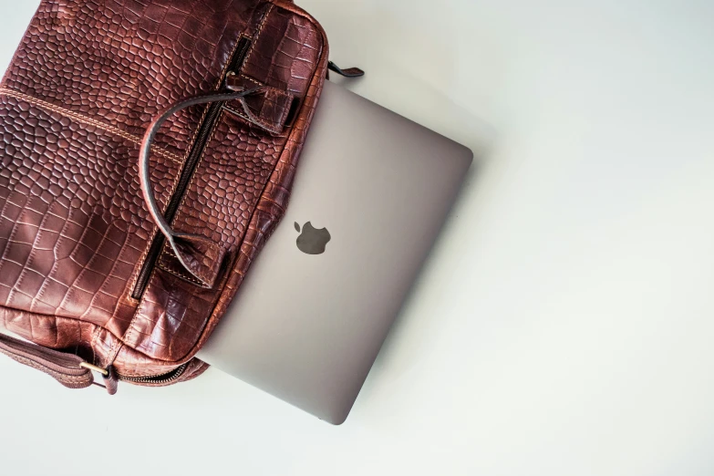 a laptop, purse and handbag on a white surface