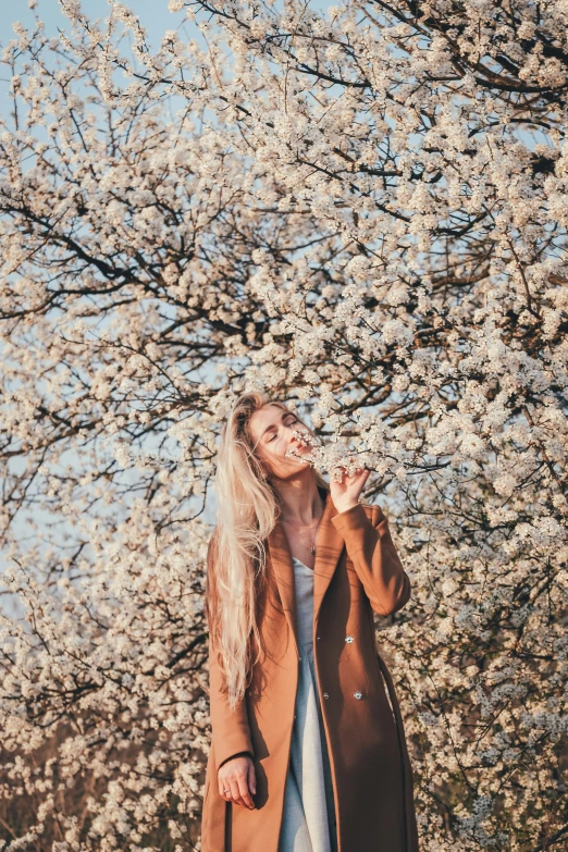 a girl wearing jeans and a jacket stands by the blossoming tree