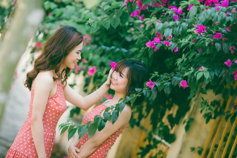 two girls standing side by side in front of pink flowers