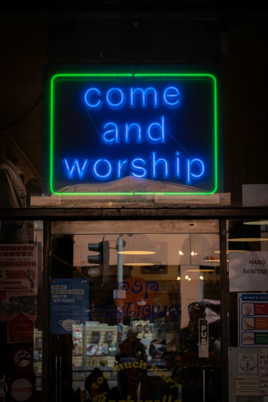 a neon sign reading come and worship sitting in front of a shop