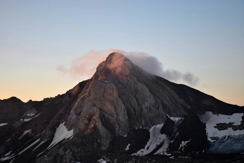 the top of a snow capped mountain has clouds in the sky