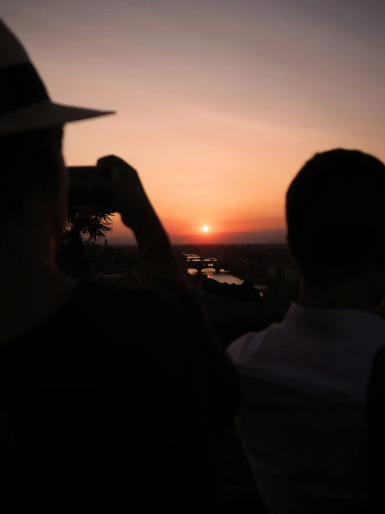 a couple of people sitting at the top of a hill watching sunset