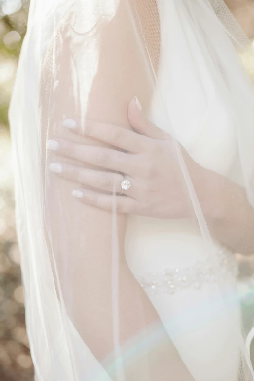 a woman wearing a white veil holds a wedding ring