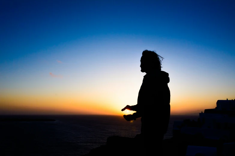 silhouette of a man with his hands crossed in front of a setting sun