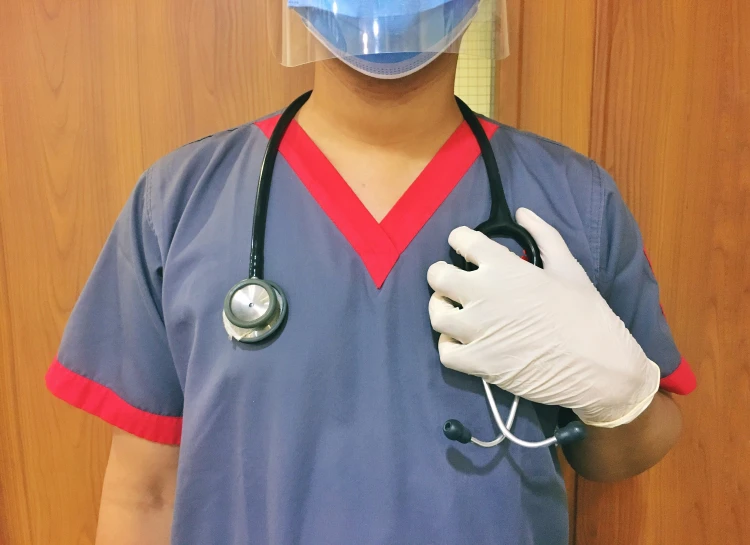 a person in scrubs, holding a stethoscope and wearing a blue surgical mask