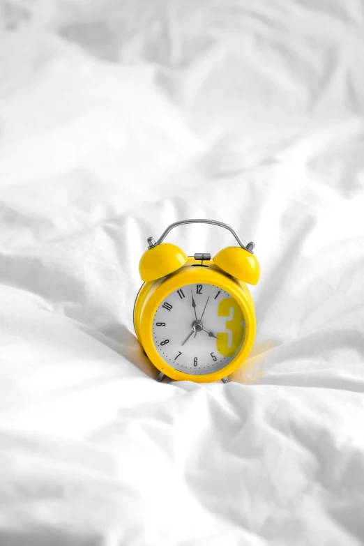 a yellow alarm clock on a white bed with white sheets