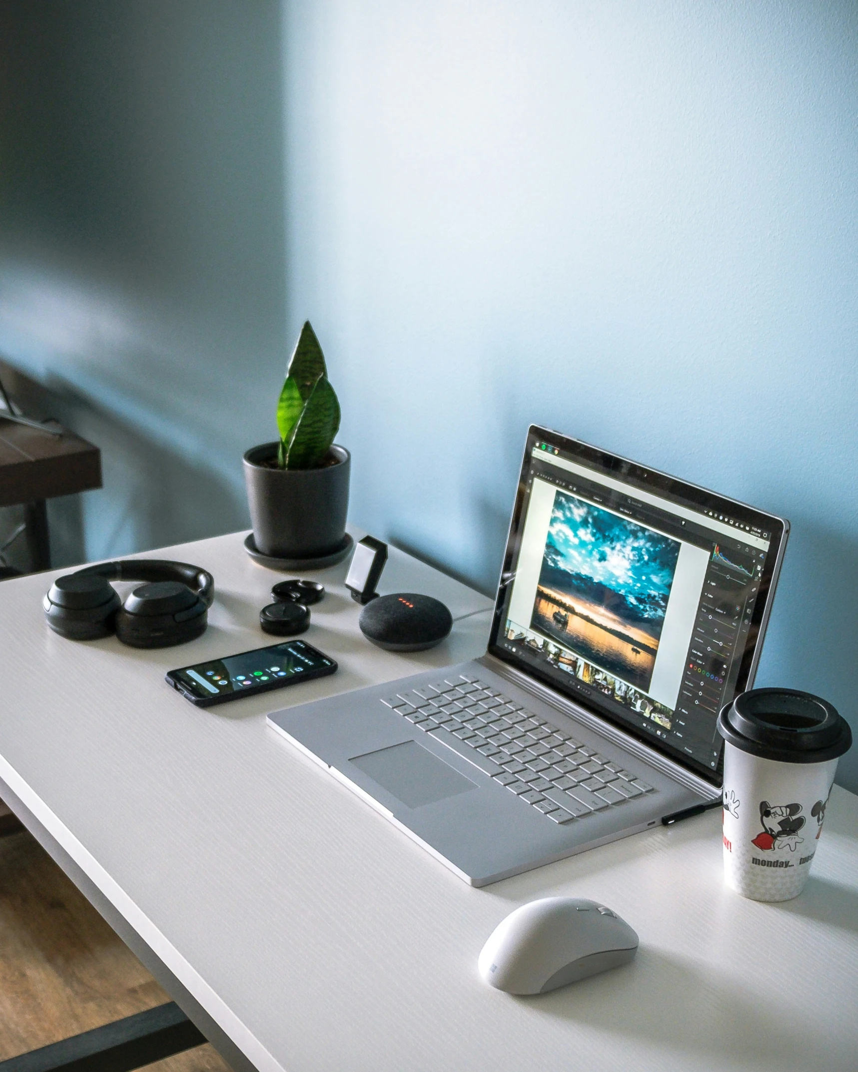 a laptop on the desk is opened with a cup of coffee, headphones and a cell phone