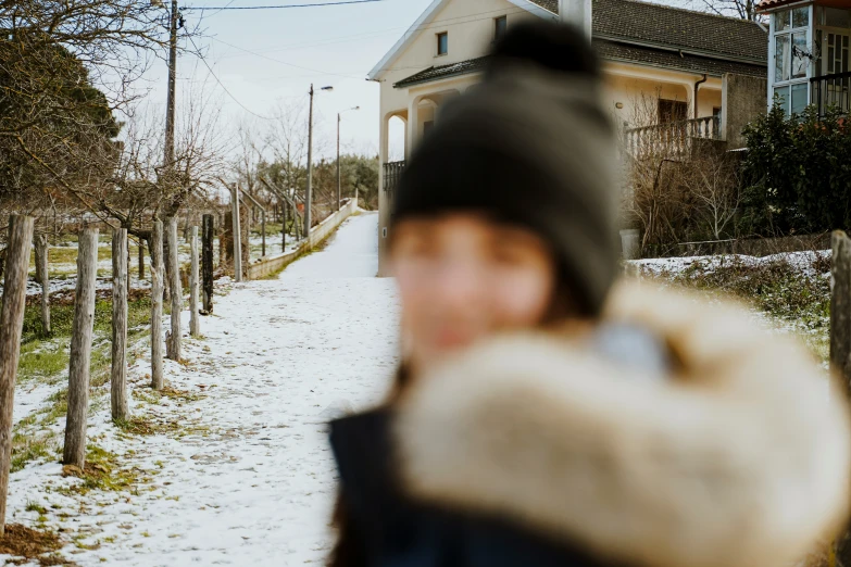 a person walking down a snowy road with a house in the background